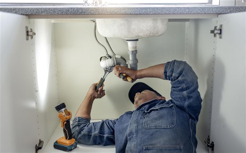 Plumber repairing pipes beneath a bathroom sink in Deltona