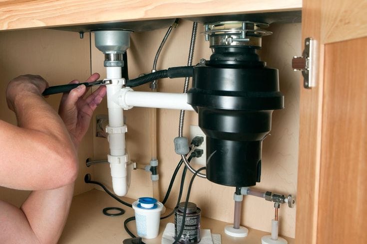 Plumber installing a garbage disposal beneath a kitchen sink in Deltona