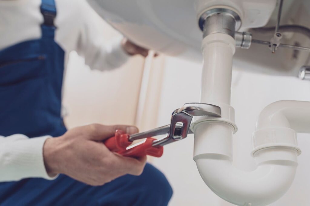 Plumber repairing a white drain pipe beneath a sink in Deltona