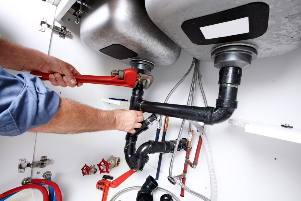 Plumber repairing drain pipes beneath a kitchen sink in Deltona